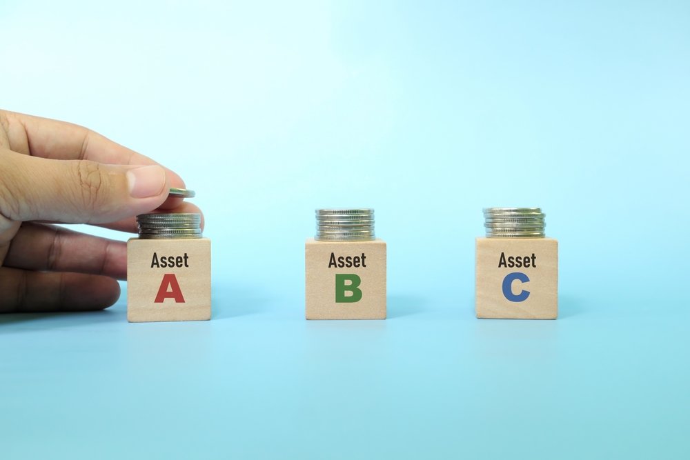 A hand places a coin on a stack labeled Asset A. Next to it are two more stacks labeled Asset B and Asset C, each with coins, against a light blue background.
